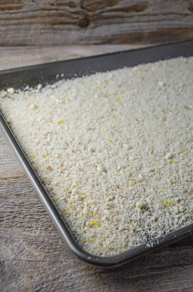 Processed bread crumbs mixed with lemon zest spread out onto a rimmed baking sheet.