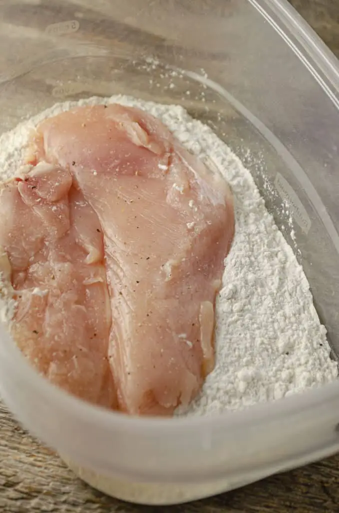 A chicken cutlet being dredged in flour.