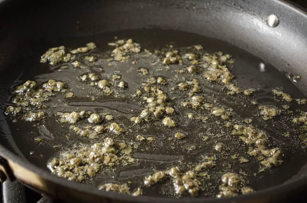 Capers frying in butter in a black non-stick skillet.