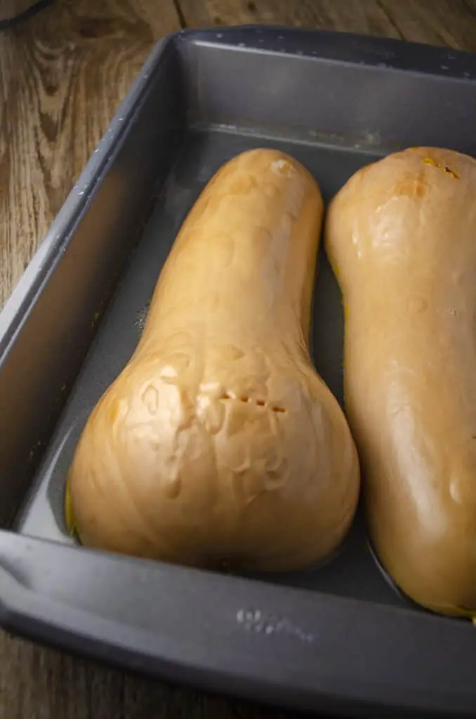 A halved and roasted butternut squash sits flat-side-down in a roasting pan with bubbly-soft skin showing it's done roasting and ready to be made into Winter Squash Pasta Sauce.