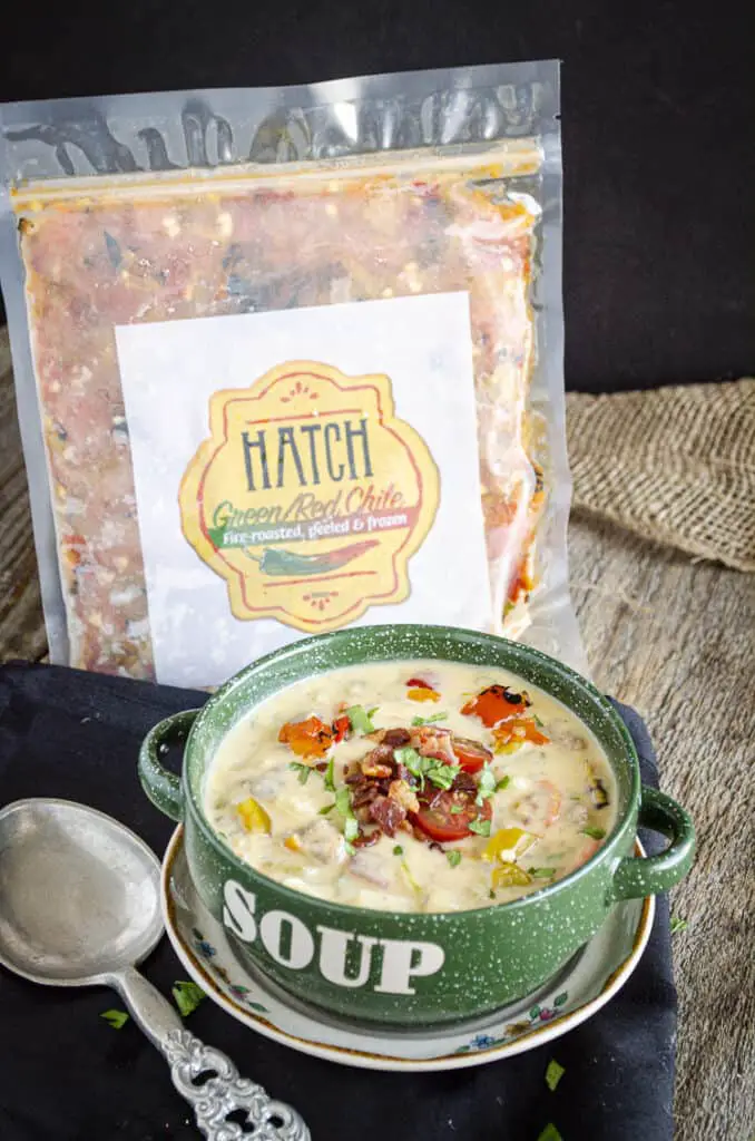 A package of chopped Hatch Green Chile sits next to a bowl of bacon cheeseburger soup sprinkled with fresh herb and sliced tomato.