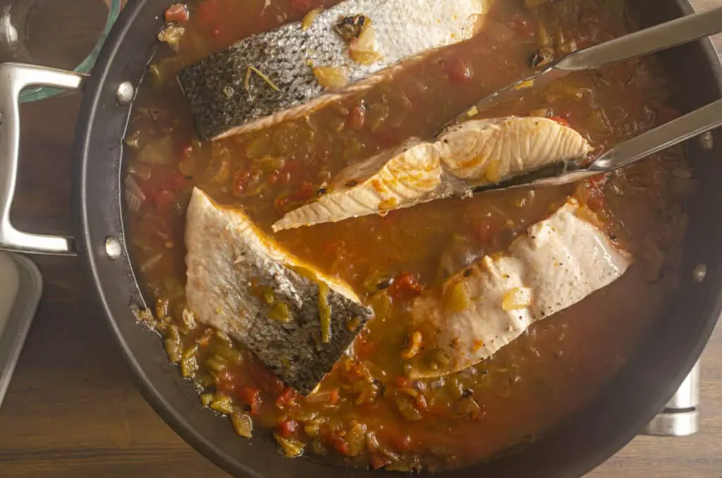 Salmon fillets are being flipped over with metal tongs in a pan full of braising liquid to make "Easy, One-Pan Salsa Poached Salmon with Mango"