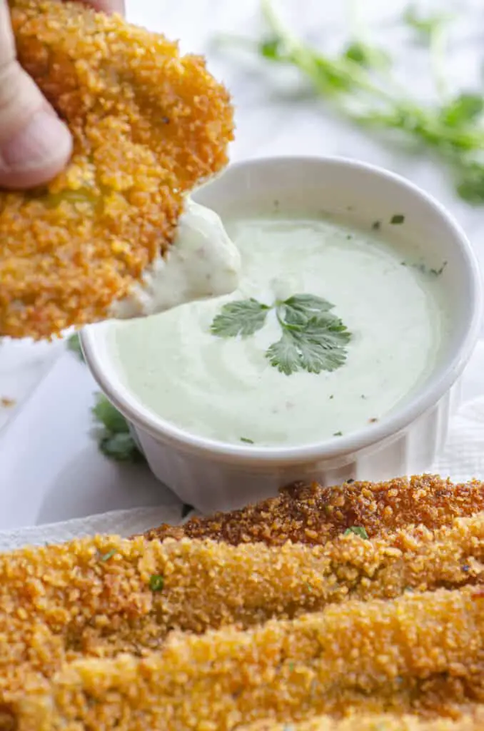 A Fried Hatch Green Chile strip is dipped into cilantro-lime crema dipping sauce.