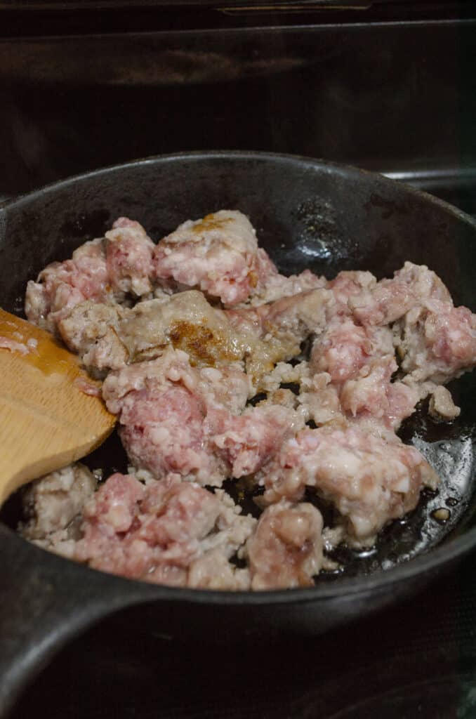 Pork sausage browns in a small black cast iron skillet on an electric stove.