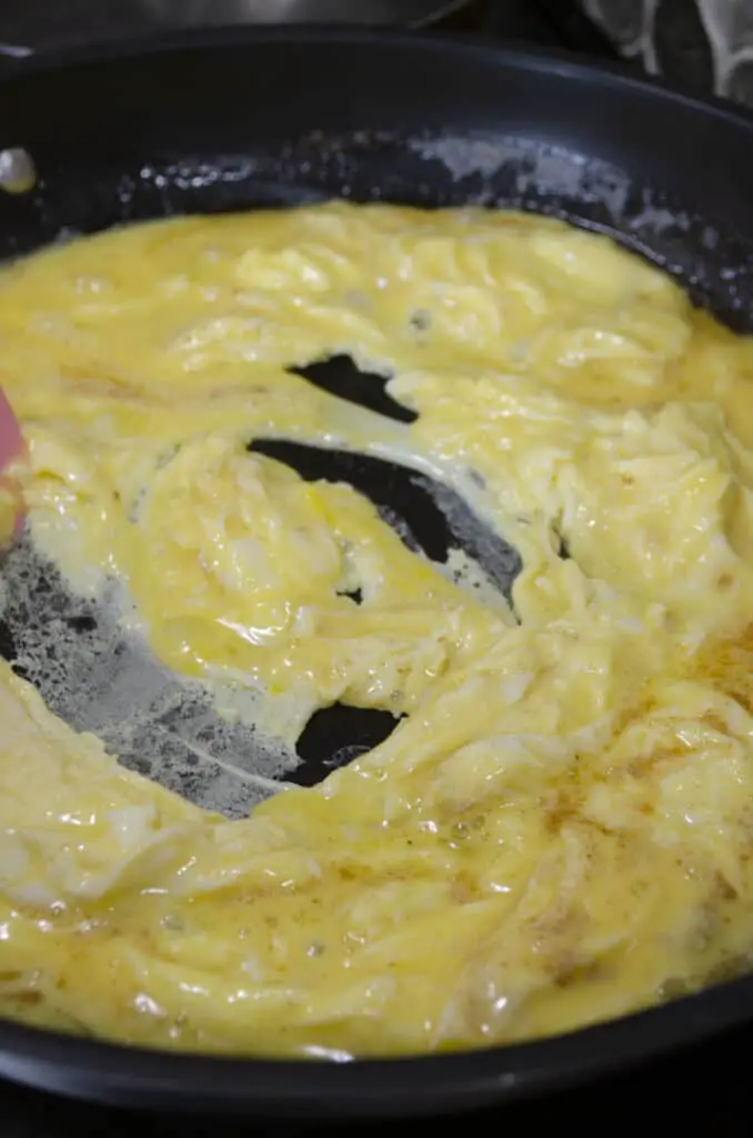 Scrambled eggs cook in a large non-stick skillet on an electric stove.