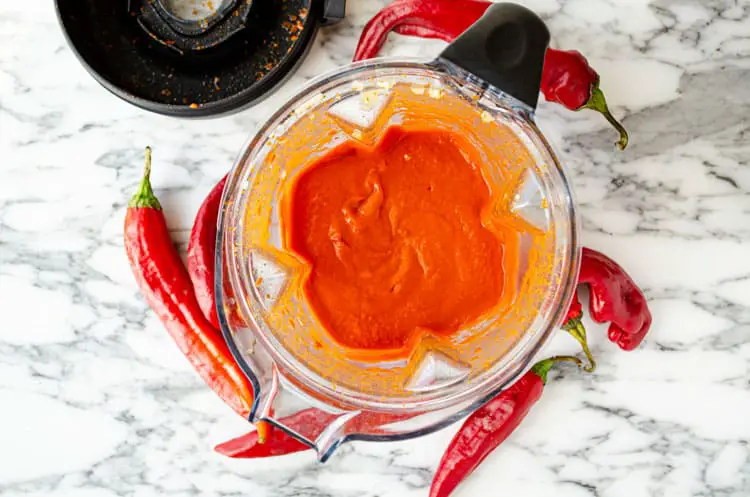 Looking down into a blender containing  just blended, reddish-orange fresh red chile sauce.