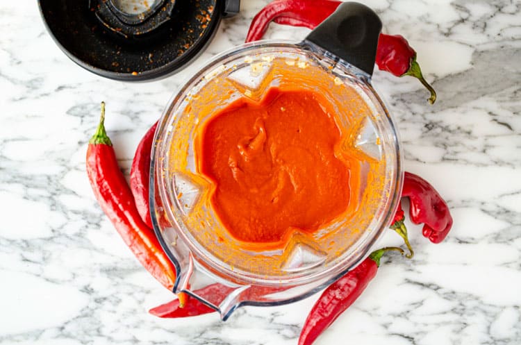 Looking down into a blender containing  just blended, reddish-orange fresh red chile sauce.