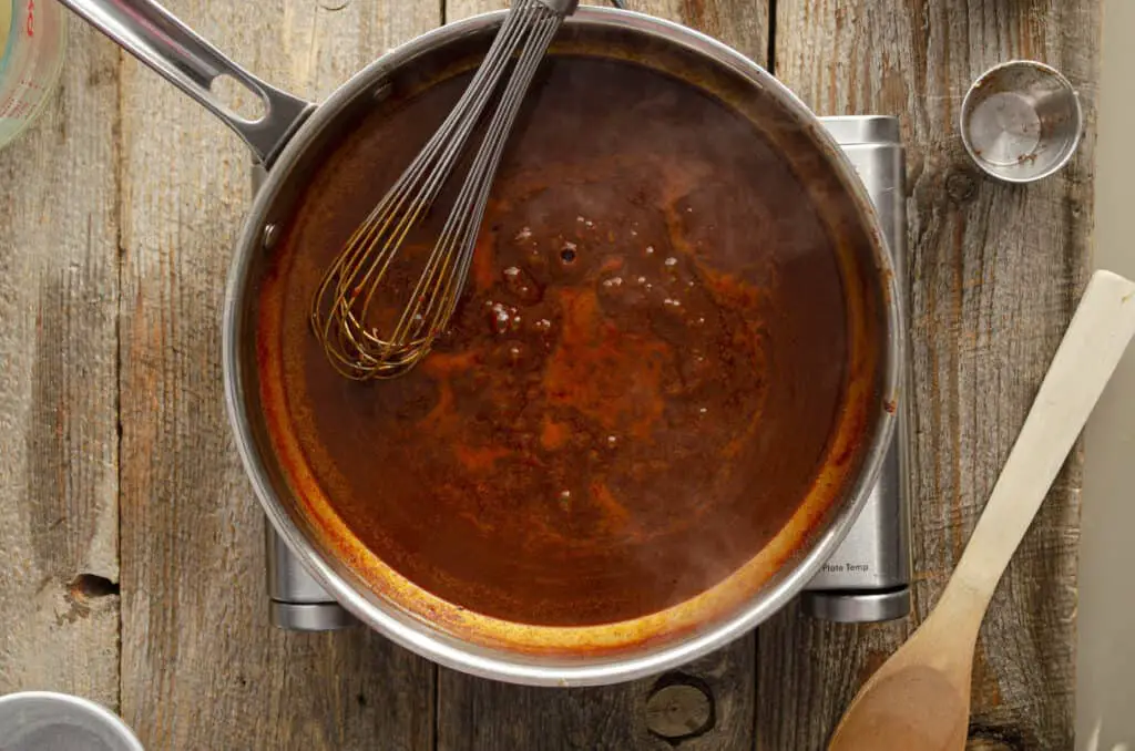 Red chile sauce simmers in a stainless steel pan .