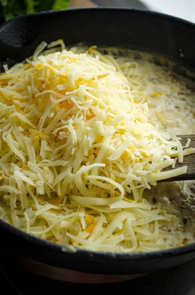 A large mound of shredded cheese is being stirred into a sauce in a cast iron skillet.