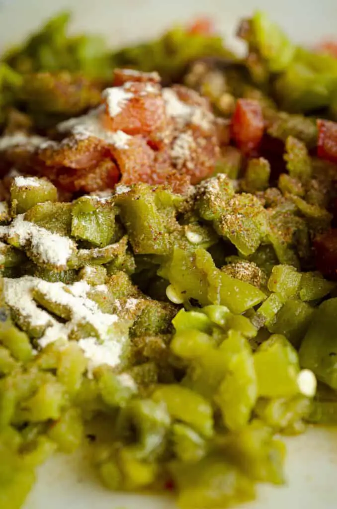 A closeup of chopped Hatch green chile and diced red tomato that have been sprinkled with dry herbs and spices, ready to be cooked into Green Chile Queso.