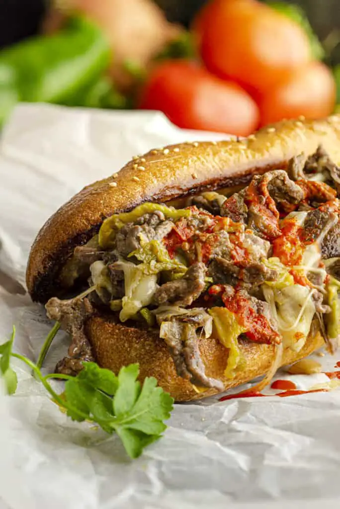A closeup of a freshly made cheesesteak sandwich made with Hatch green chile, and drizzled with red Hatch chile sauce.