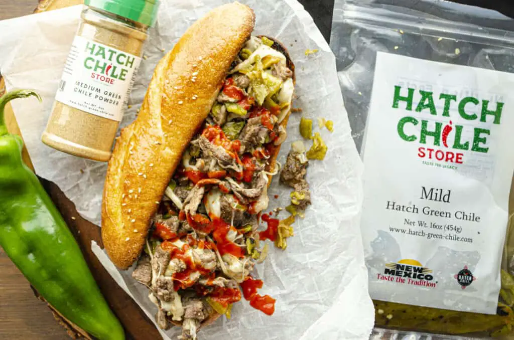 Looking down at a cheesesteak sandwich surrounded by Hatch Chile Store green chile products.