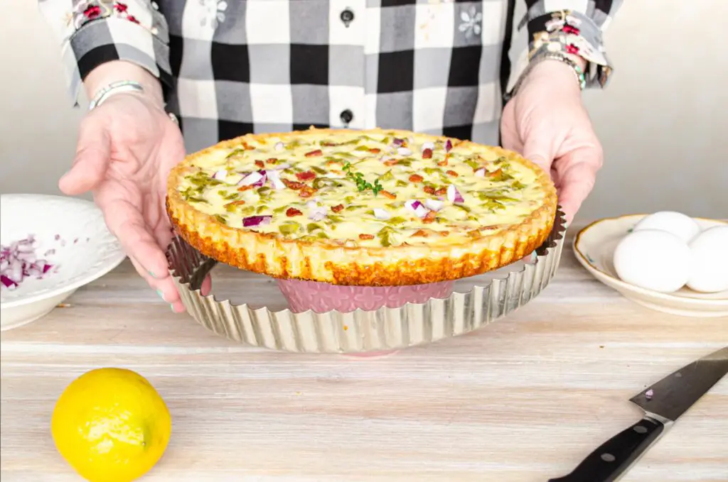 A tart pan's outer ring is removed to display a quiche and it's fluted crust.