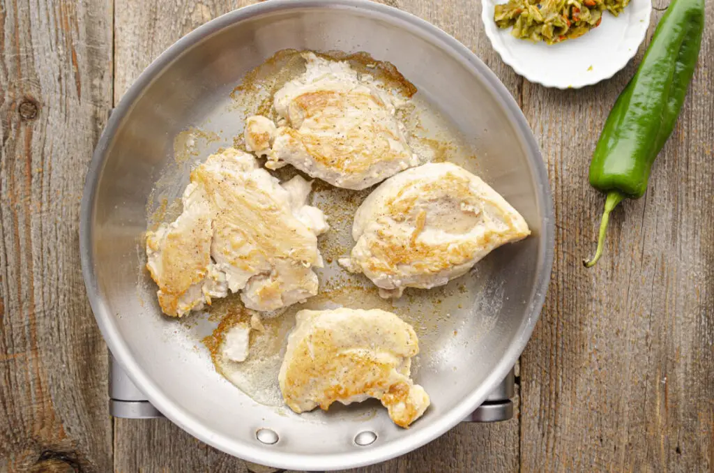 Looking down onto a stainless steel skillet sauteing four golden-brown chicken breasts.