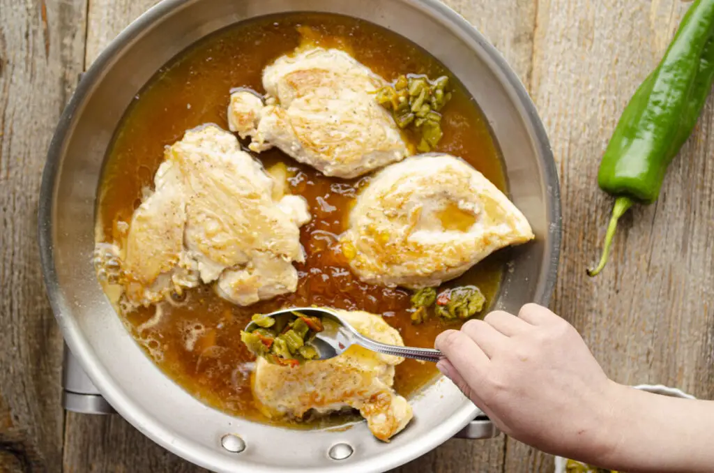 Placing spoonfuls of roasted chopped Hatch green chile into skillet with chicken and glaze.