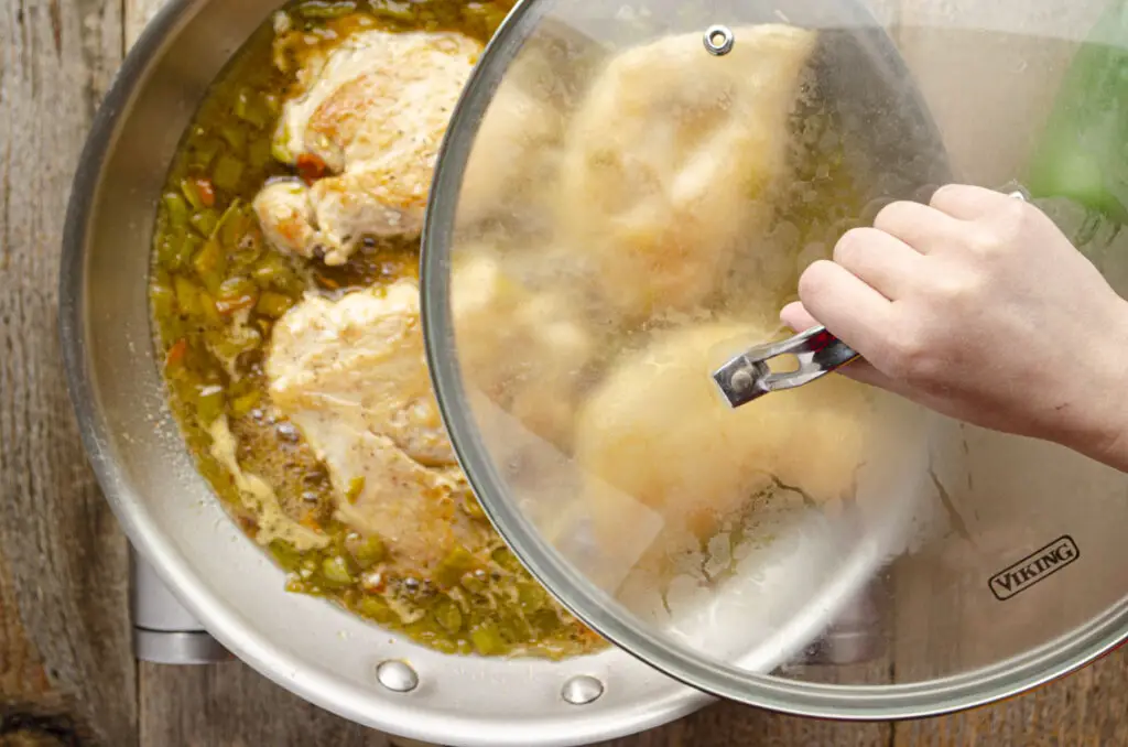 A lid is being placed over the skillet of chicken and glaze.