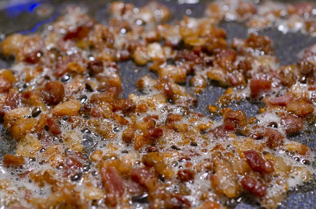 A closeup picture of chopped bacon browning in a nonstick skillet.