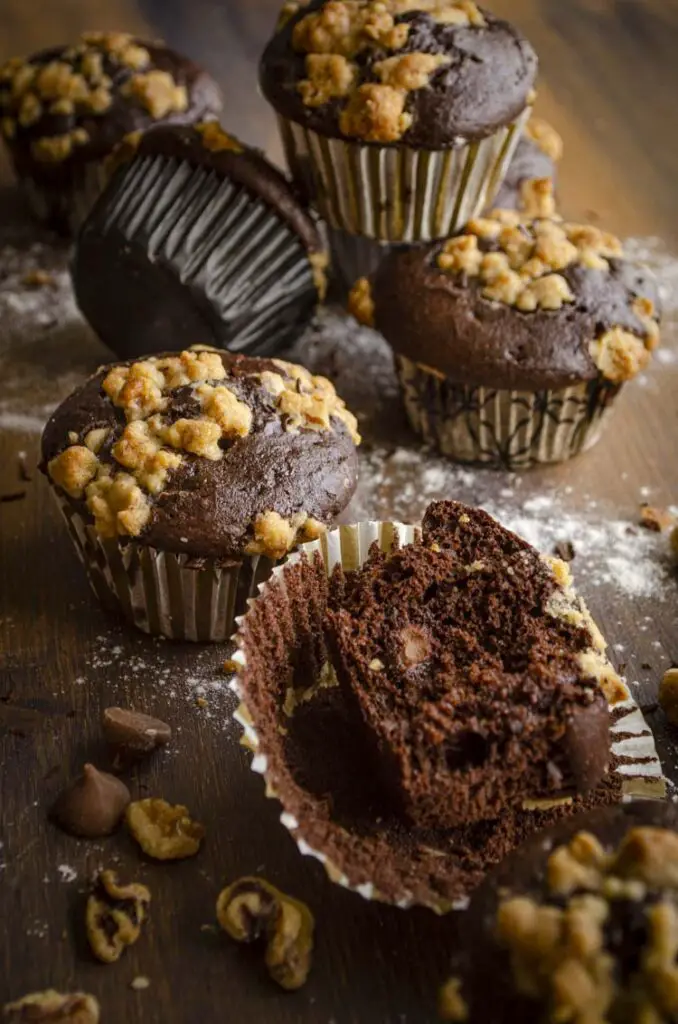 A pile of chocolate Johnny Depp Trial Muffins rests on a wooden table with one partially eaten, showing the interior.