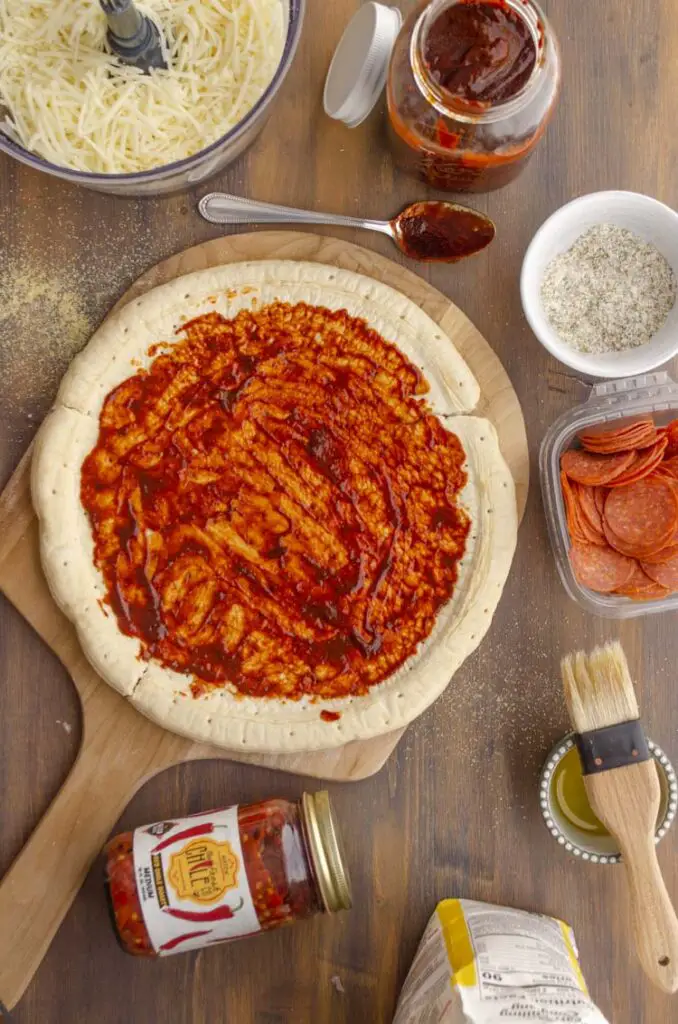 Hatch Red Chile sauce is spread over a round pizza dough ready to be covered with cheese and toppings.