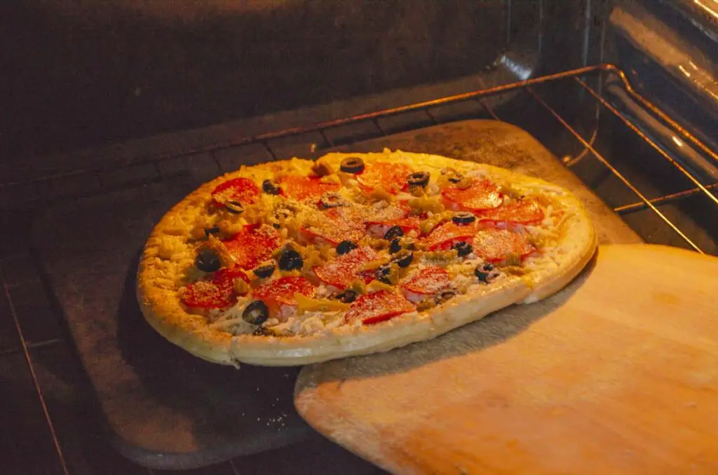 A pizza is being slid into an oven onto a baking stone.