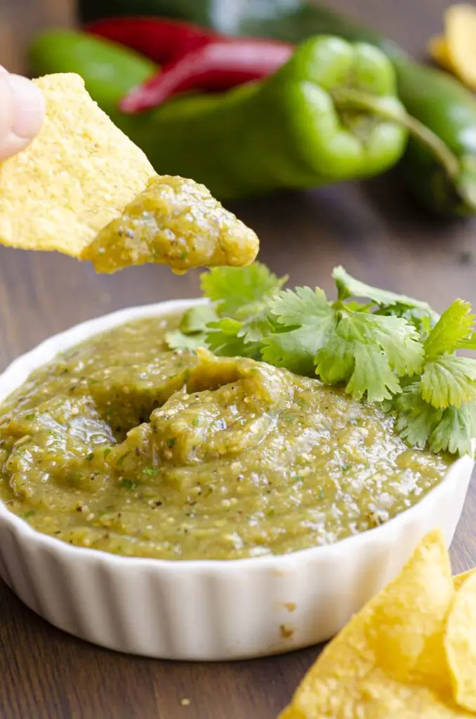 A bowl of Salsa Verde with a tortilla chip held above.