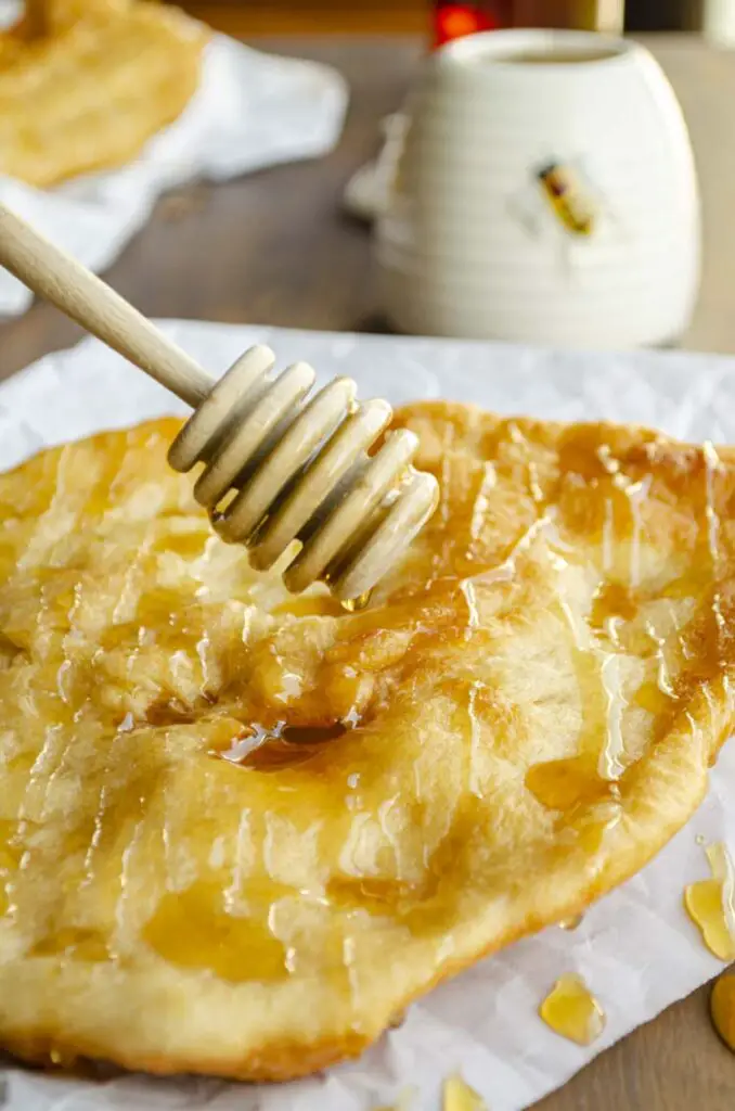 A golden fried piece of Indian Frybread is drizzled with honey from a honey wand.