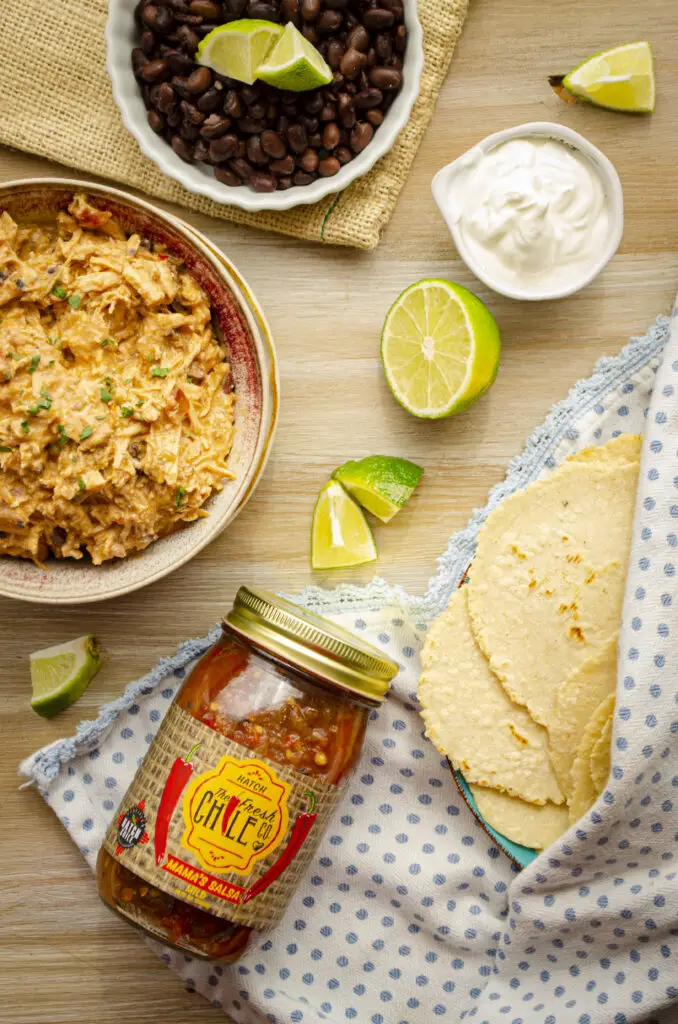 Looing down onto a wooden tabletop with all the ingredients displayed to make Instant Pot Shredded Salsa Chicken, along with some freshly homemade corn tortillas.