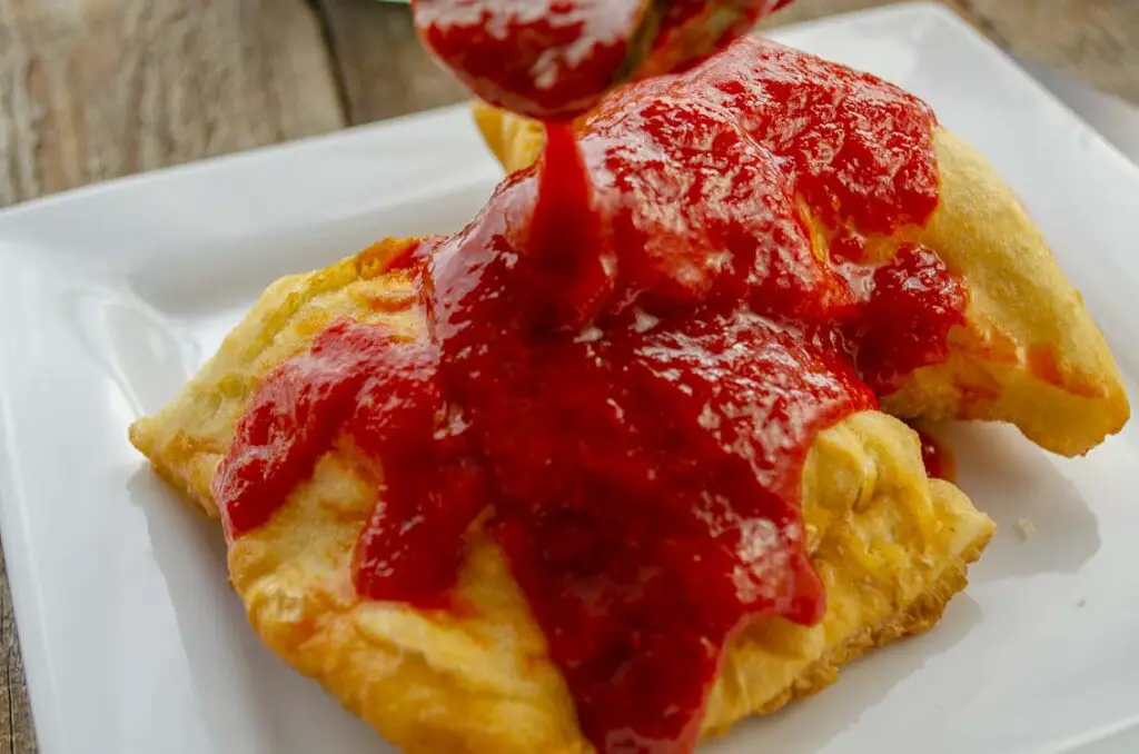 Two stuffed sopapillas placed on a white plate have red chile sauce poured over them.