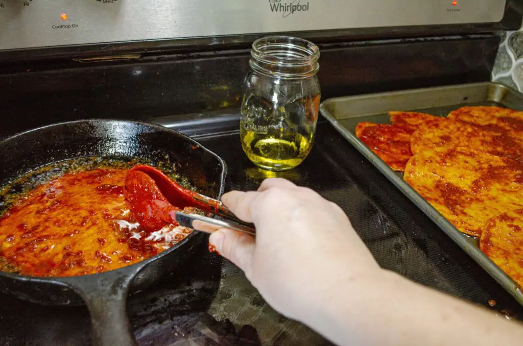 Someone uses tongs to dip a red chile soaked corn tortilla into hot frying oil on a stovetop.