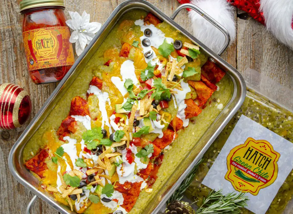 Christmas Style enchiladas in a stainless steel casserole dish covered in garnishes. Packages of Hatch chile surround.