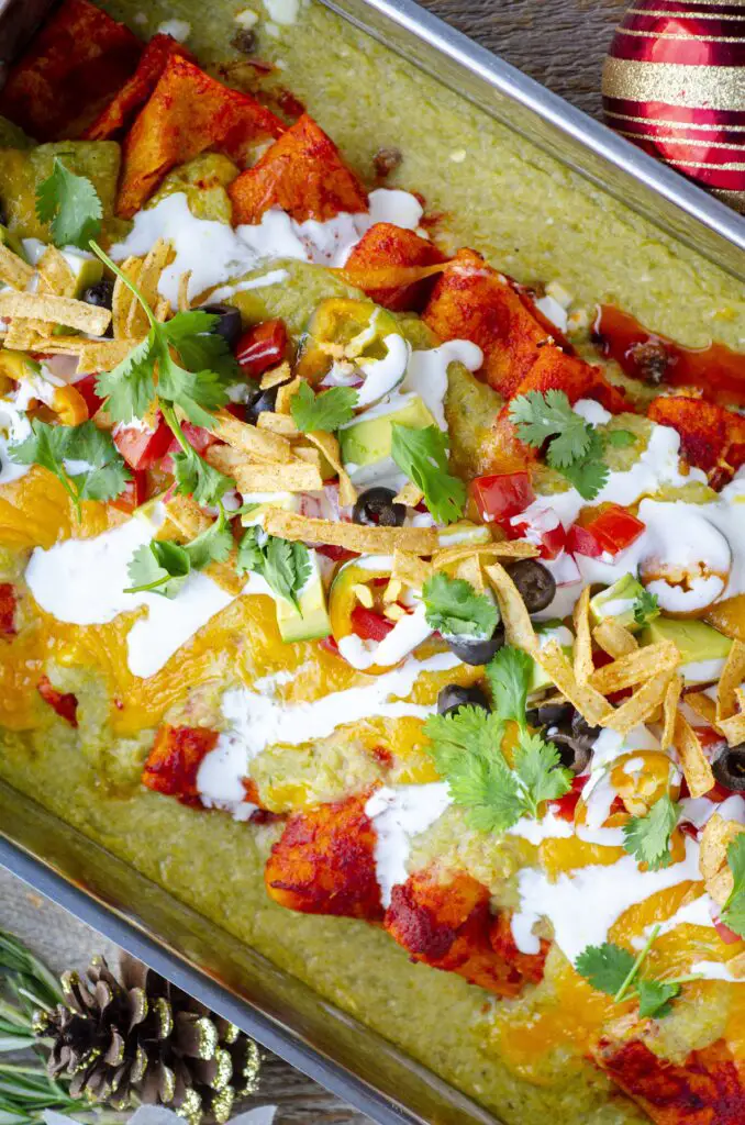 A closeup of the garnishes placed on a freshly baked pan of Christmas enchiladas. Diced tomato, diced jalapeno, diced avocado, crispy tortilla strips, crema and fresh cilantro leaves.