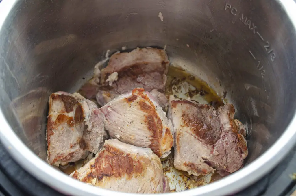 Chunks of pork brown in the bottom of an instant pot pressure cooker