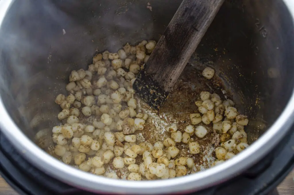 Hominy is cooked with dried herbs and seasonings in the bottom of a pressure cooker.
