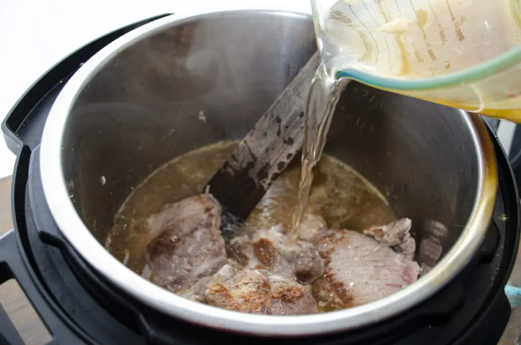 Broth is added to meat in a pressure cooker.