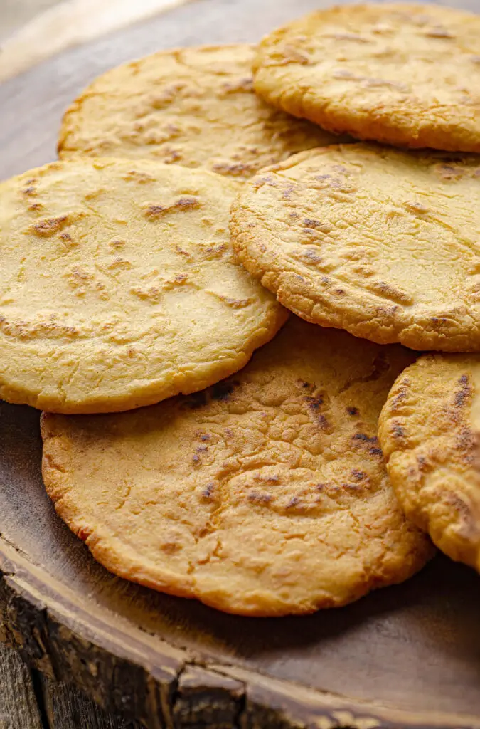 Several golden-fried gorditas not yet stuffed with filling, sit on a wooden table.