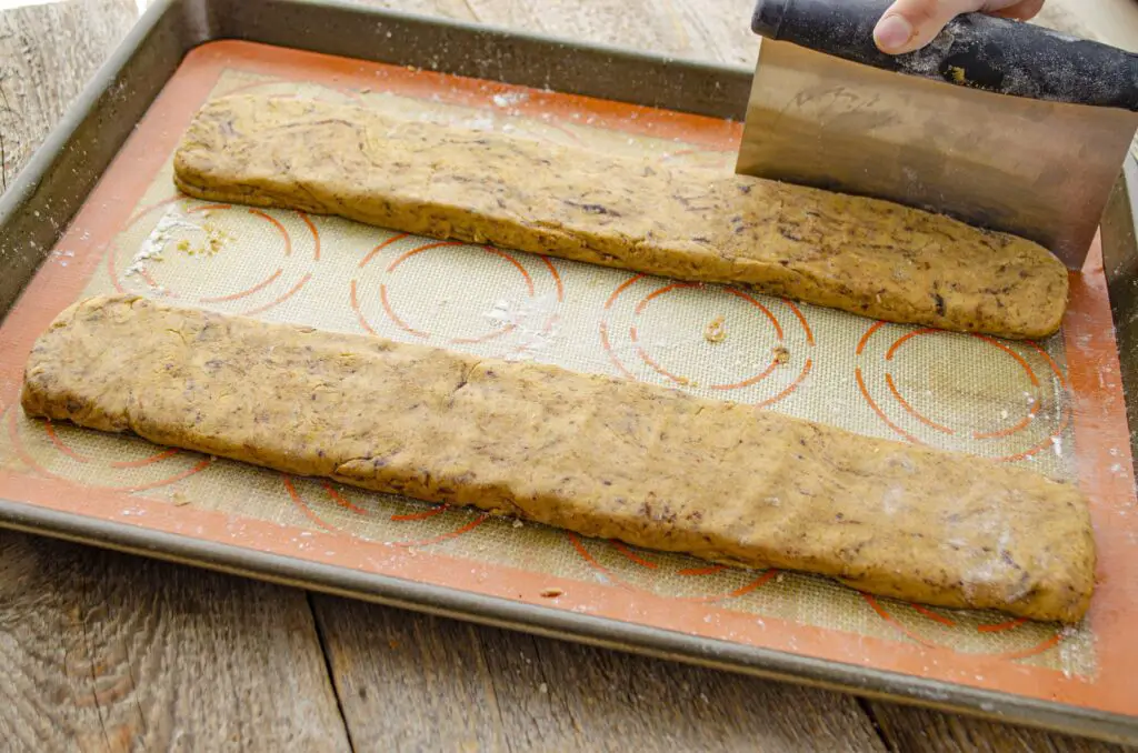 Two pieces of biscotti dough shaped into long thin rectangles on a cookie sheet.