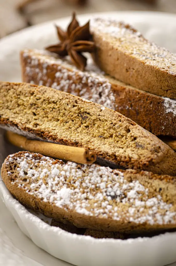  A closeup picture of several pieces of Christmas Spice Biscotti showing their texture. A Cinnamon stick and star anise pod are intermingled with the biscotti piecees.