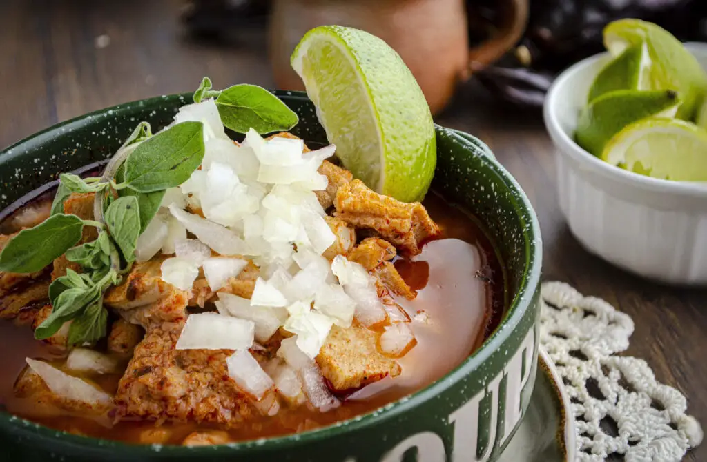 A delicious bowl of hot menudo garnished with onion and a lime wedge.