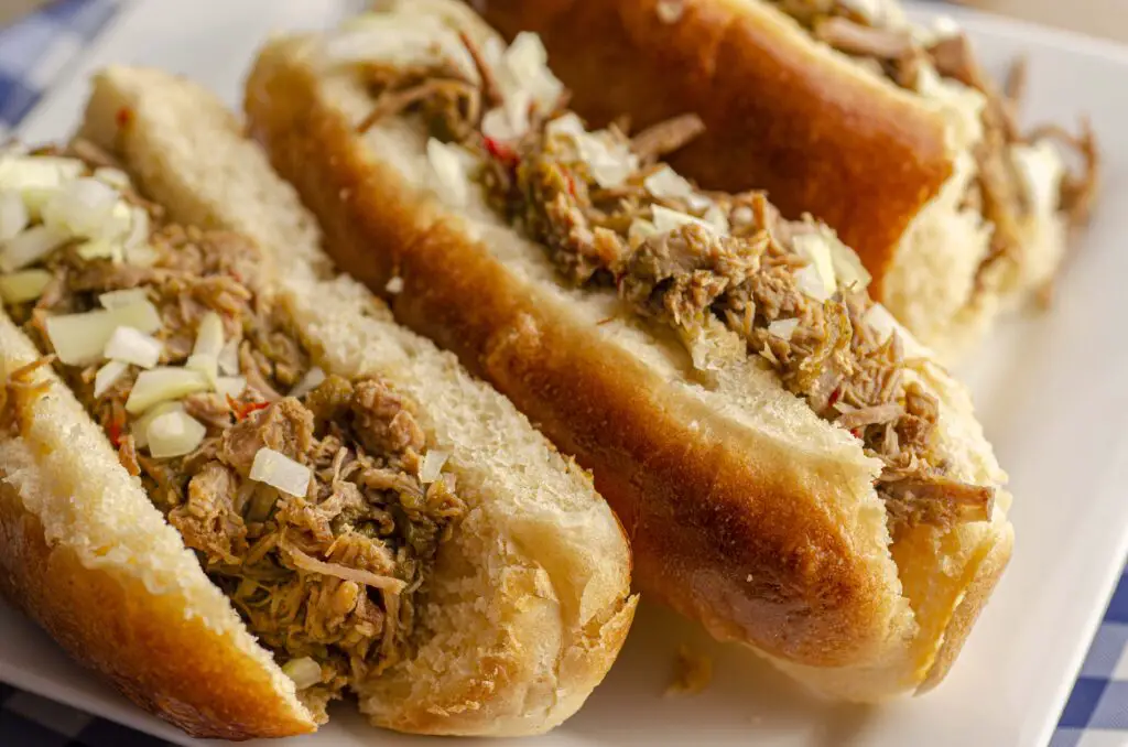 Three homemade buns are stuffed with Instant Pot Green Chile pulled pork and are garnished with freshly diced white onions.