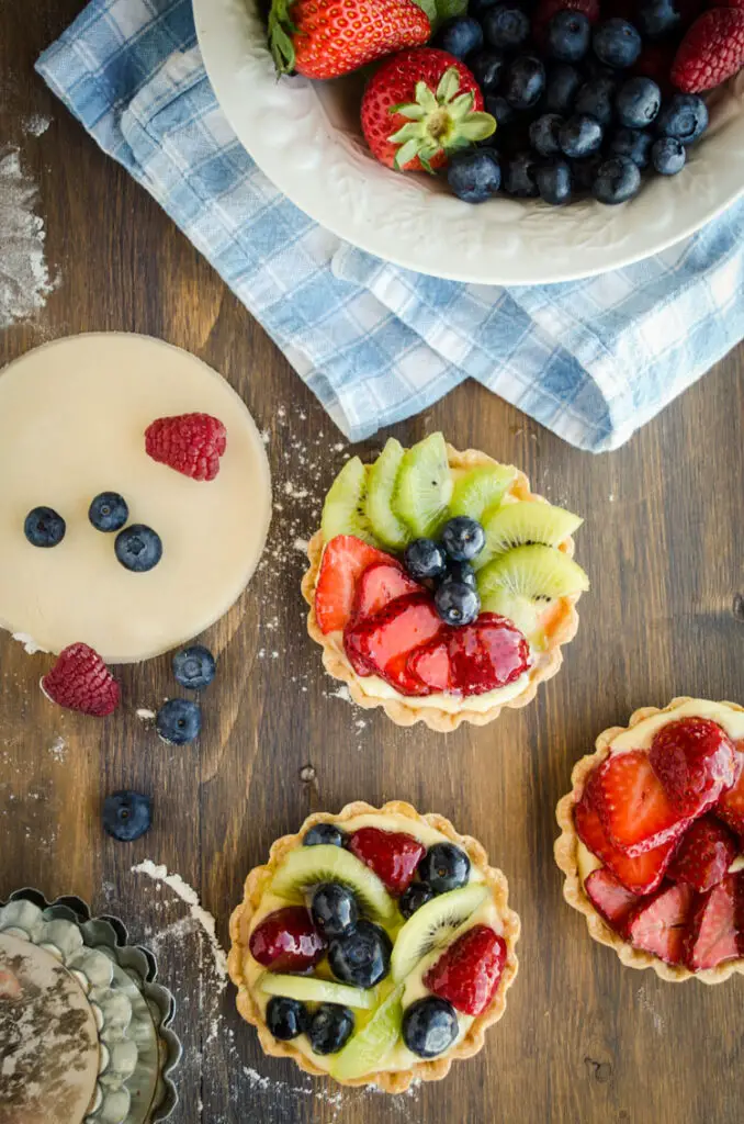 Looking down on a wooden table showing a bowl of fresh fruit a three small fruit tarts.