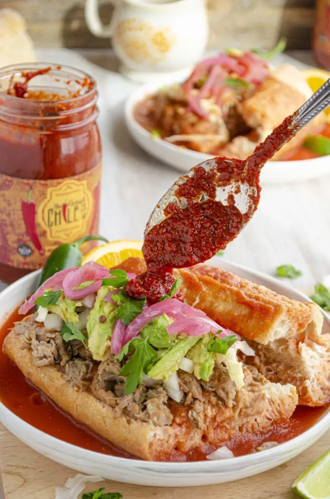 A dollop of red Hatch chile sauce is placed on an open faced tortas ahogadas sandwich.