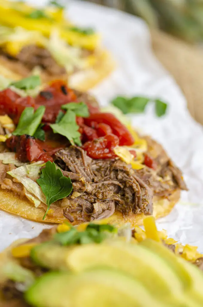 A close-up picture of barbacoa meat on a tostada, showing the moist texture of the meat and its spices.