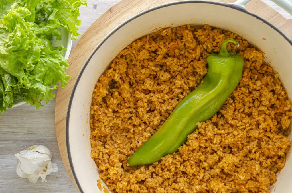 A large white dutch oven is filled with Mexican rice and has a large Hatch chile nestled into the center.