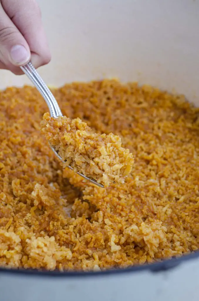 A fresh batch of Mexican rice is fluffed with a fork.