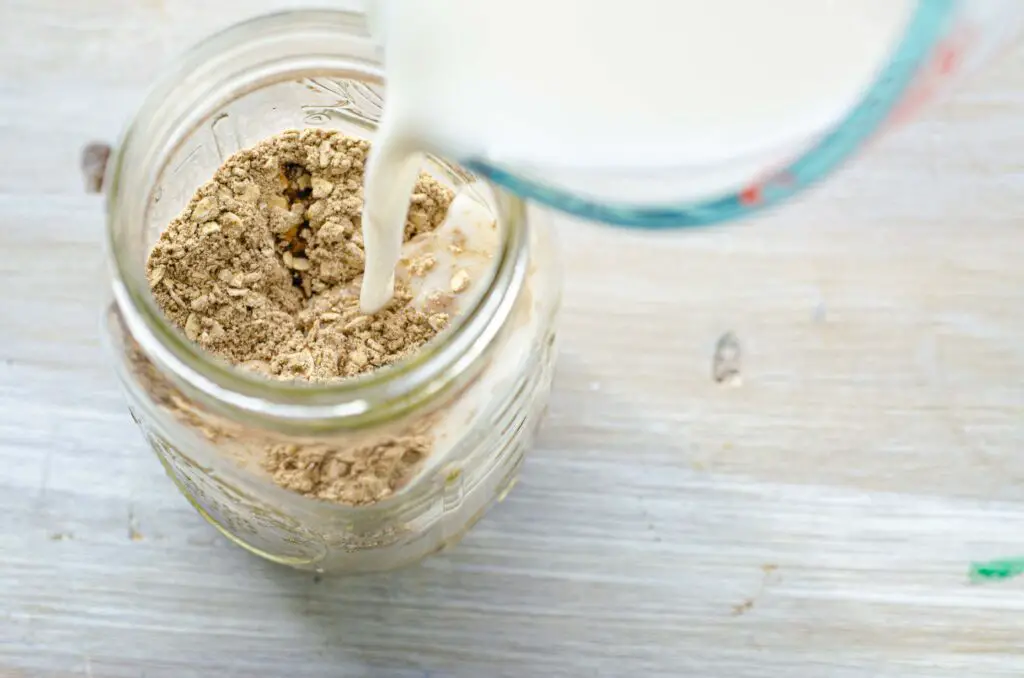 Looking down into a Mason jar with powdered Naked Oats at the bottom and has milk being poured in from the top.