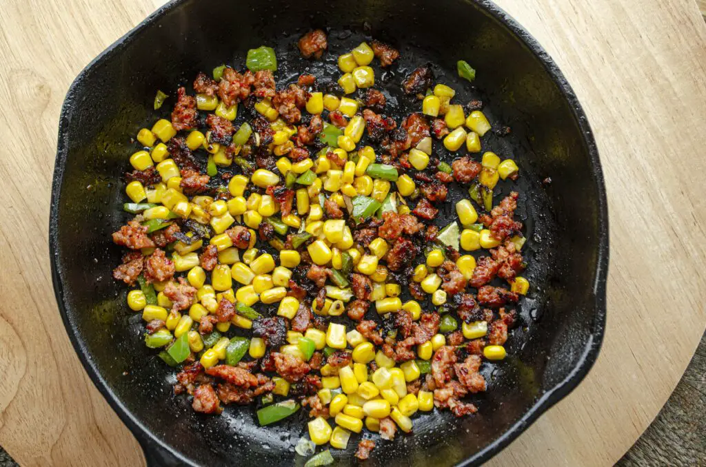 Looking down into a black cast-iron skillet with cooked corn, choizo, and chopped green chile.