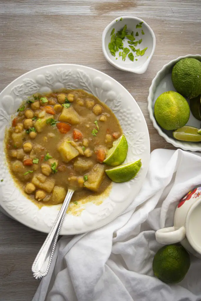 A bowl of coconut curry stew featuring canned chickpeas is garnished with fresh lime slices and minced cilantro.