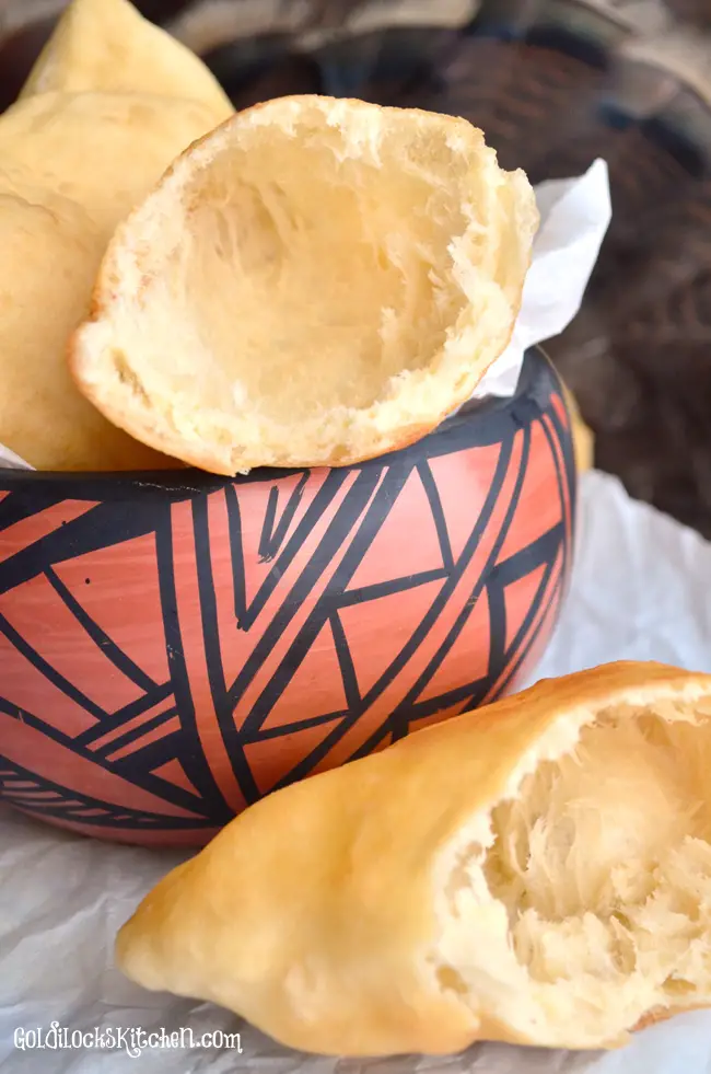 A red and black painted southwestern pot displays a New Mexican sopapilla that has been broken open to show it is hollow inside.