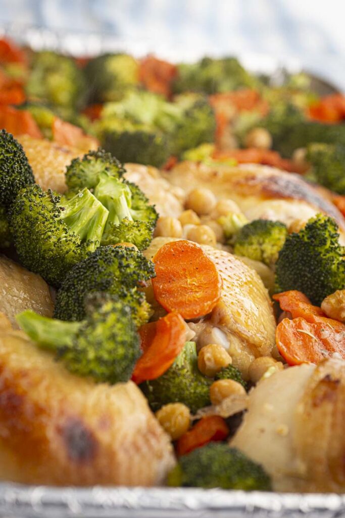 A closeup of roasted Honey Chicken Thighs with veggies on a rimmed baking sheet hot out of the oven.