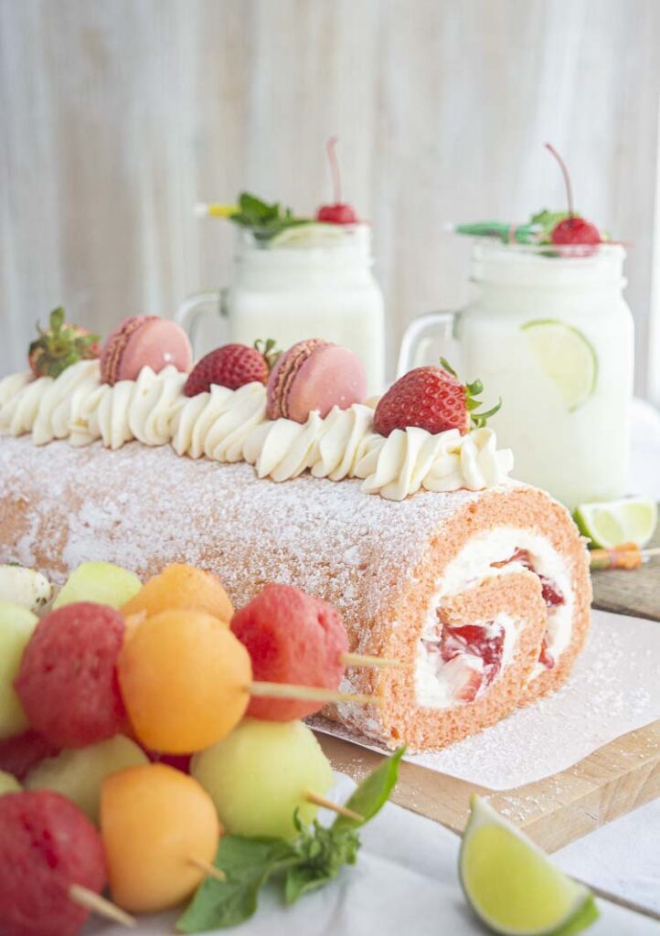 An Easter brunch table setting with Party Fruit Skewers, a Strawberry Cream Cake Roll cake, and  mason jar mugs filled with Brazilian Lemonade topped with fresh fruit garnishes.